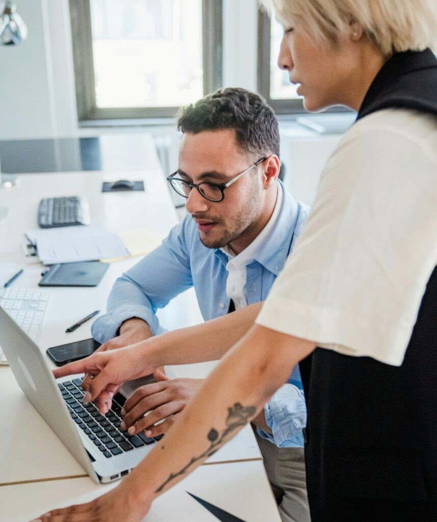 Deux collègues collaborant devant un ordinateur portable dans un bureau lumineux, en train d’échanger sur un projet.