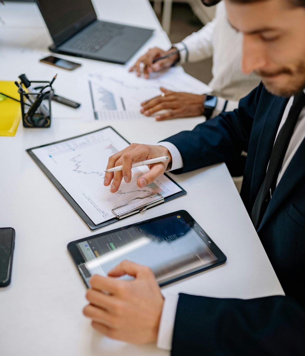 Deux professionnels en réunion analysant des graphiques financiers sur tablette et documents imprimés dans un cadre de travail moderne.