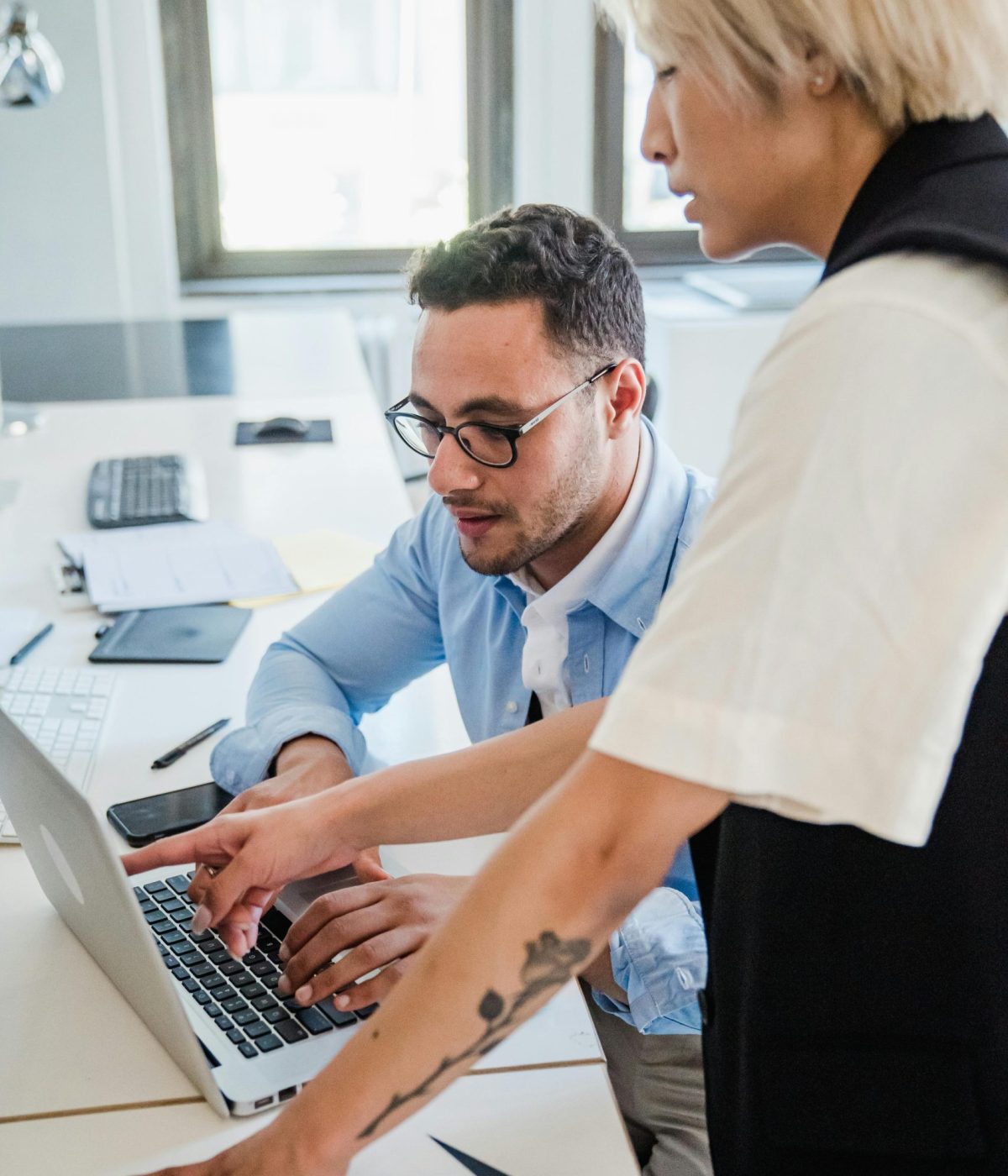 Deux collègues collaborant devant un ordinateur portable dans un bureau lumineux, en train d’échanger sur un projet.